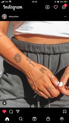 a woman with tattoos on her arm and hand holding something in her other hand while wearing sweatpants