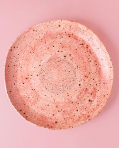 a pink plate with speckles on it sitting on a pink surface in front of a white background