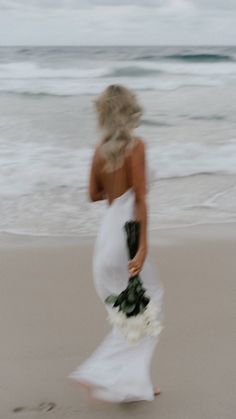 a woman in a white dress is walking on the beach