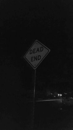 a black and white photo of a dead end sign in the dark with cars behind it