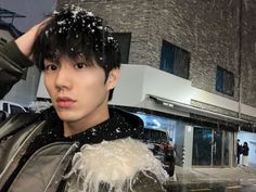 a man standing in front of a building with snow on his head and hands behind his head