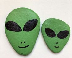 two green rocks with faces painted on them, one has an alien face and the other has black eyes