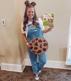 a girl in overalls is holding a book and wearing a giraffe mask