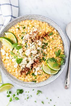 a bowl filled with corn and garnished with cilantro, limes, and parmesan cheese