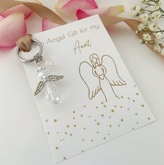 an angel keychain sitting on top of a card next to pink roses and flowers