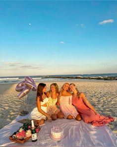 three women are sitting on the beach and having a picnic with their cake, balloons and confetti