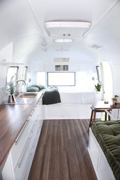 the interior of a camper with wood flooring and white walls, including a bed