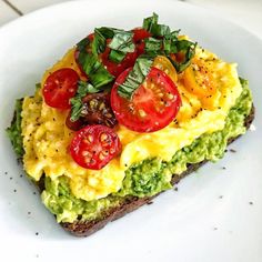 an omelet with tomatoes, avocado and other toppings on a white plate