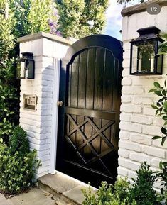 an open door to a white brick house with green bushes and trees in front of it