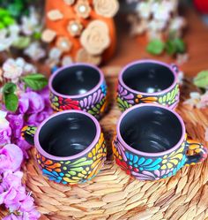 three colorful cups sitting on top of a woven basket next to purple and white flowers