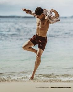 a shirtless man kicking a frisbee on the beach in front of the ocean