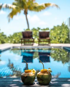 two coconuts sitting on top of a wooden table next to a pool with chairs