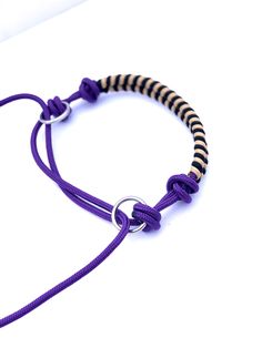 a purple and black cord bracelet with an oval clasp on the end is attached to a white background