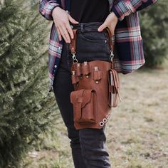 a woman is holding a brown purse in her hands while standing next to a tree