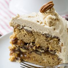 a piece of cake with white frosting and pecans is on a plate next to a fork