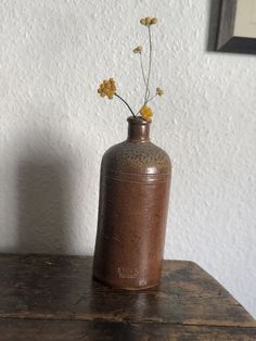 a brown vase with yellow flowers in it on a wooden table next to a white wall