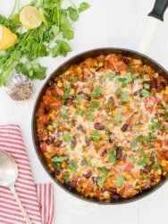 a skillet filled with mexican food and garnished with cilantro, limes, corn, and parsley