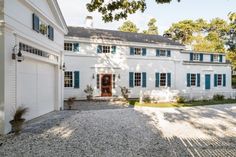 a large white house with blue shutters on the front and side doors, surrounded by gravel