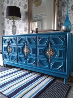 a blue dresser sitting on top of a rug next to a lamp and a mirror