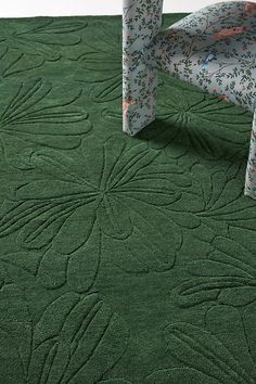 a green area rug with an intricate design on the top and bottom, in front of a chair