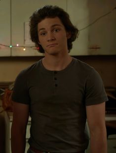 a young man standing in a kitchen looking at the camera with an intense look on his face