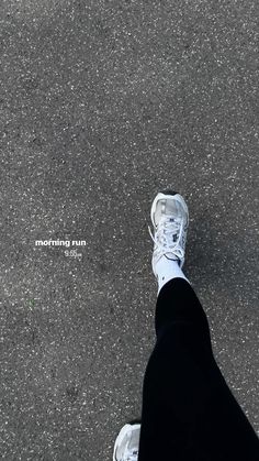 a person wearing white sneakers and black pants standing on the pavement with their feet in the air