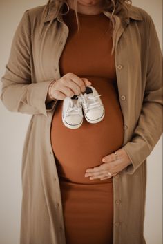 a pregnant woman is holding her shoes in front of her belly while wearing a brown dress