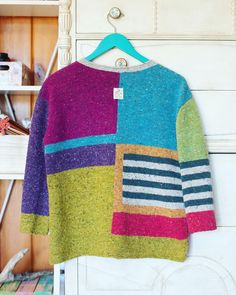 a multicolored sweater hanging on a clothes hanger in front of a white dresser