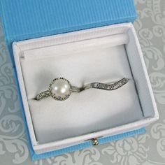 Timeless and classic, this vintage inspired pearl engagement ring and curved wedding band set are reminiscent of the Edwardian era when fine metalwork was designed with intricate details and delicate settings that were fashioned to resemble the patterns of fine lace. The vintage style Edwardian-inspired pearl ring is handcrafted from recycled sterling silver where a lightly oxidized floral band is set with a luminous 8-8.5mm cultured creamy white freshwater pearl in a filigree heart-crown settin Elegant Wedding Ring With Classic Design, Elegant Round Band Bridal Sets For Wedding, Elegant Bridal Sets With Round Band For Wedding, Classic Pearl Wedding Ring, Elegant Wedding Rings With Pearl Drop, Elegant Gold Wedding Ring With Classic Design, Wedding Pearl Drop Ring With Diamond, Elegant Pearl Drop Rings For Wedding, Classic Pearl Ring For Wedding