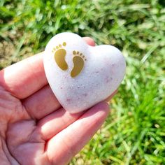 a hand holding a heart shaped rock with footprints painted on it in front of green grass