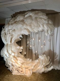 a large white feather wreath with lights hanging from it's sides and curtains in the background