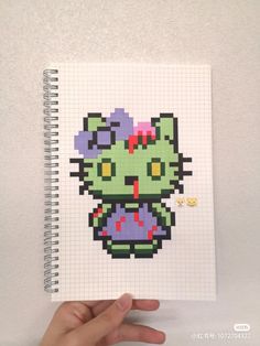 a hand holding up a notebook with an image of a hello kitty in pixel art