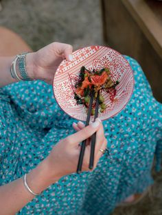 a woman holding a plate with sushi on it and chopsticks in her hand