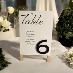 a table number sign sitting on top of a white table cloth covered table with flowers