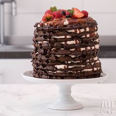 a chocolate cake with strawberries and cream on top sitting on a white pedestal in front of a kitchen sink