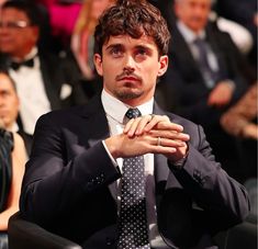 a man wearing a suit and tie sitting in front of an audience with his hands folded