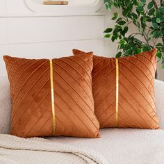 two brown pillows sitting on top of a white couch next to a potted plant