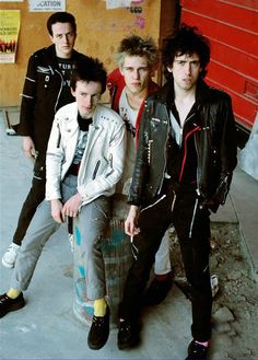 four young men standing next to each other in front of a red building with graffiti on it