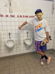 a young man standing next to two urinals in a public men's bathroom