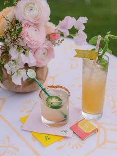 two cocktails sitting on top of a table next to vases filled with flowers