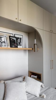 a bed with white linens and pillows in a room that has built - in cabinets