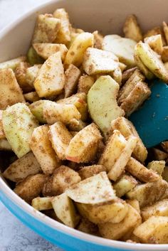 a blue bowl filled with fried potatoes and seasoning next to a wooden spatula