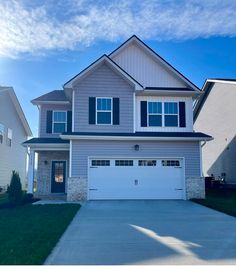 a two story house with garage in the foreground and grass on the other side