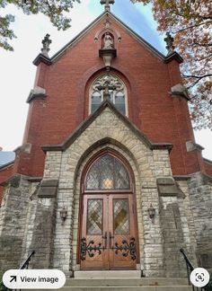 an old brick church with stained glass doors and cross above the door is surrounded by trees