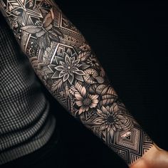 a man's arm covered in black and white tattoos, with flowers on it