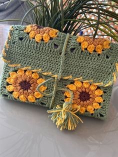 a crocheted purse with sunflowers on it and a plant in the background