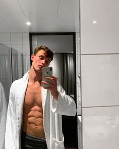 a shirtless man taking a selfie in the mirror with his cell phone and towel