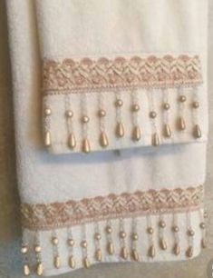 two white towels hanging up on a towel rack with buttons and beads attached to it