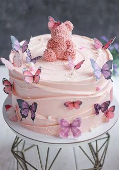 a pink cake with butterflies on it and a teddy bear sitting on top of the frosting