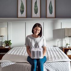 a woman sitting on top of a bed holding an air conditioner